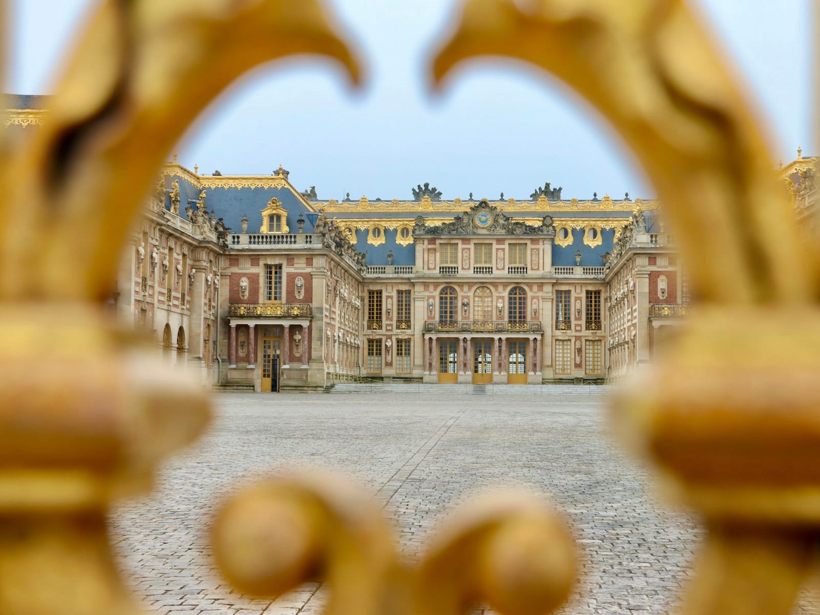 L'ingresso principale del Palazzo di Versailles incorniciato da elaborati cancelli dorati, con un ampio cortile in acciottolato che conduce alla celebre facciata del palazzo.