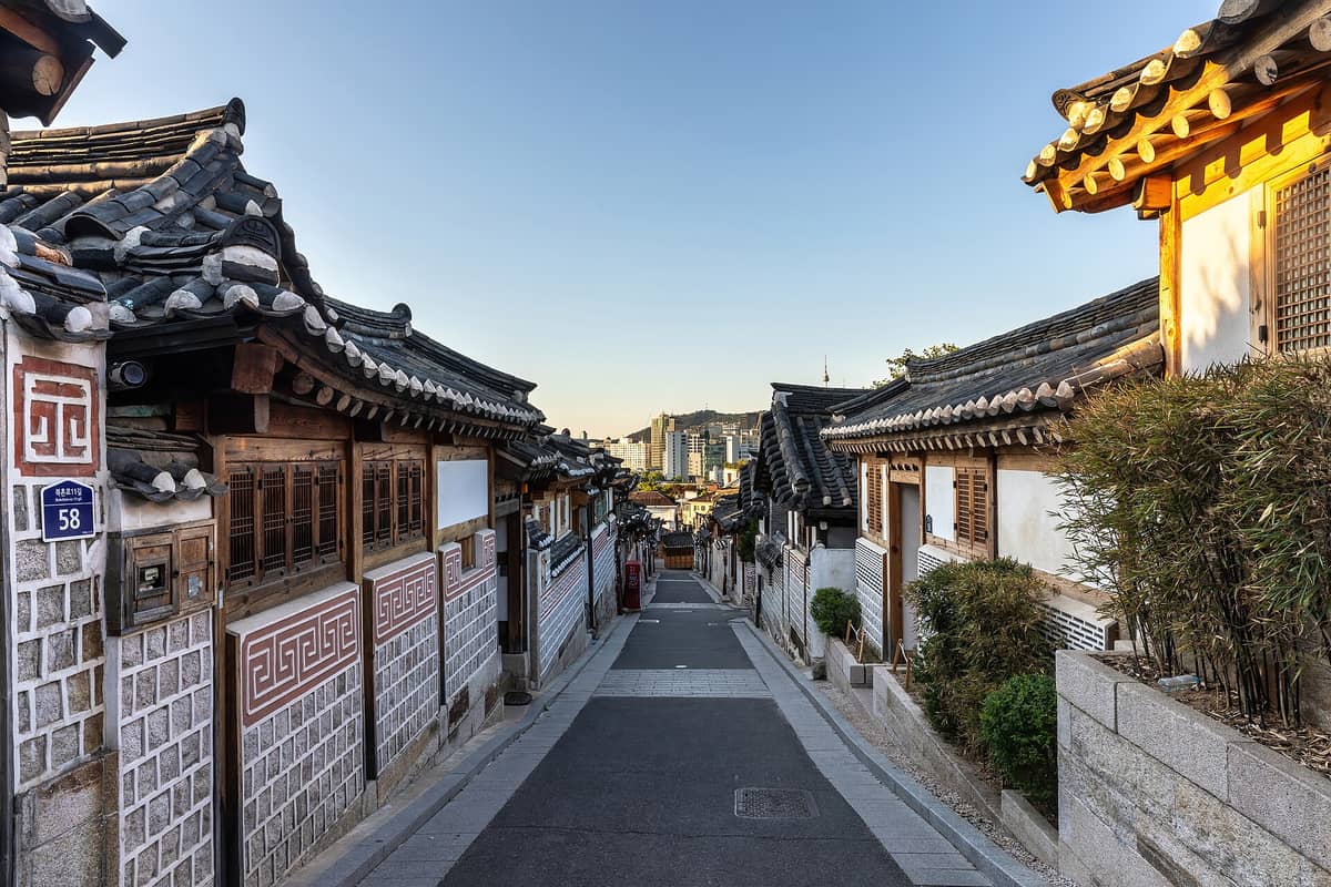 Casas hanok tradicionais alinhadas em uma rua estreita com vista para o moderno horizonte de Seul, provavelmente em Bukchon Hanok Village perto dos palácios.