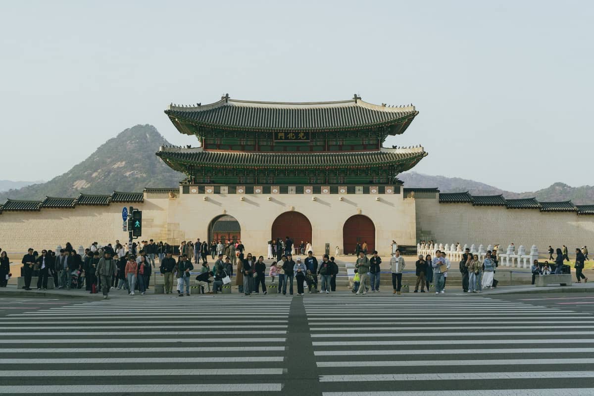 Vista ampla do portão Gwanghwamun com uma multidão de pessoas e montanhas ao fundo em Seul, marcando a entrada principal do Palácio Gyeongbokgung.