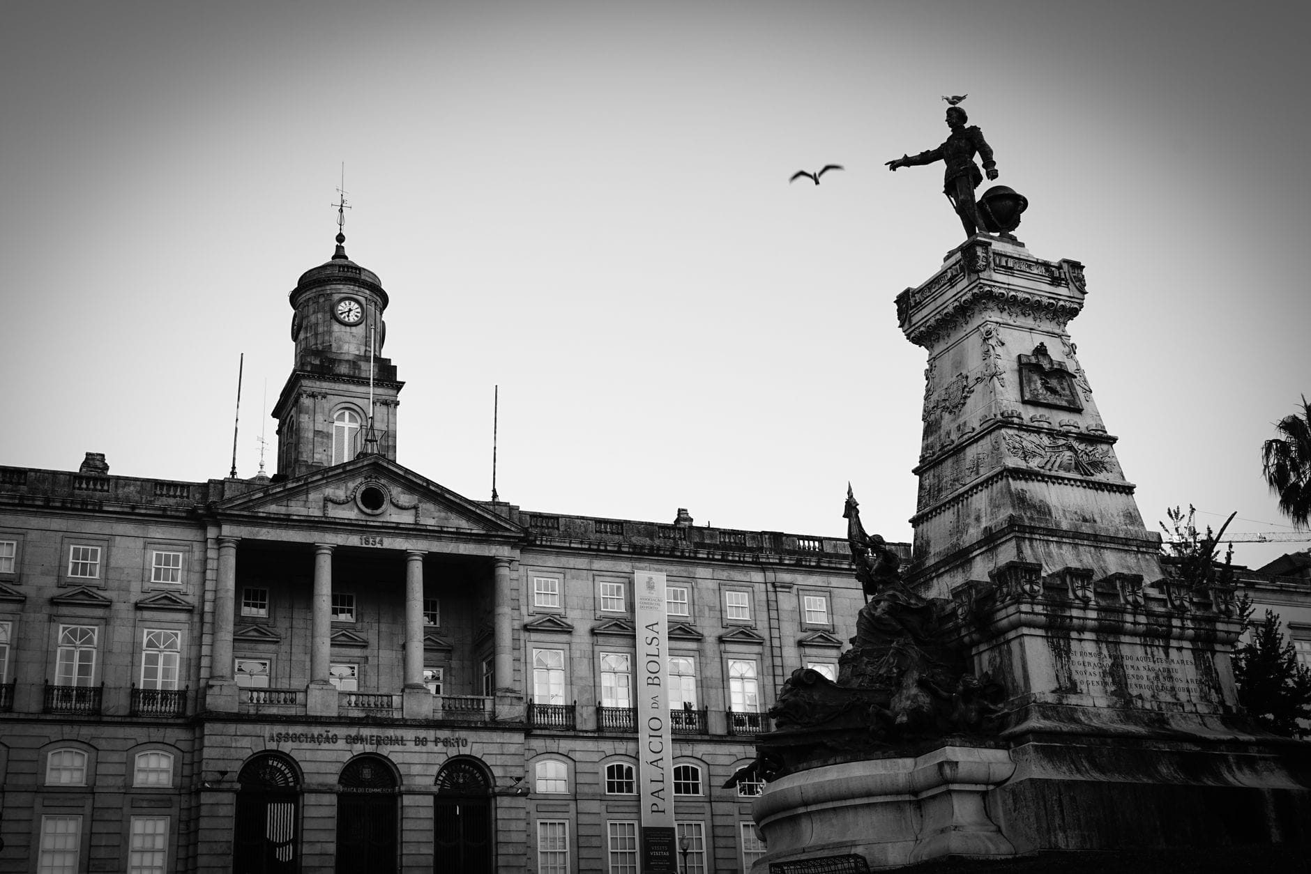 Immagine in bianco e nero della facciata neoclassica del Palácio da Bolsa con una statua imponente e una torre dell'orologio, Porto, Portogallo.