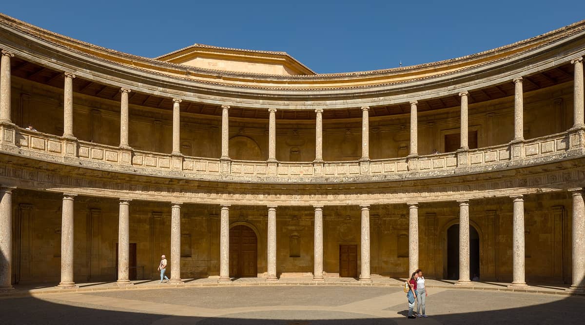 มุมกว้างของลานวงกลมภายใน Palacio de Carlos V แสดงระเบียงสองชั้นและเสาเรียงรายใต้ท้องฟ้าสีครามในเขตอัลฮัมบรา