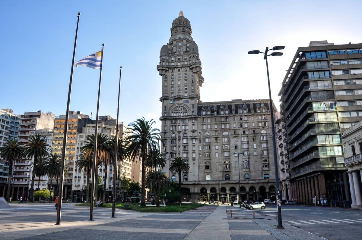 มุมกว้างของ Palacio Salvo ที่มอนเตวีเดโอจาก Plaza Independencia เห็นหอคอยสวย ต้นปาล์ม และทิวทัศน์เมืองใต้ท้องฟ้าแจ่มใส