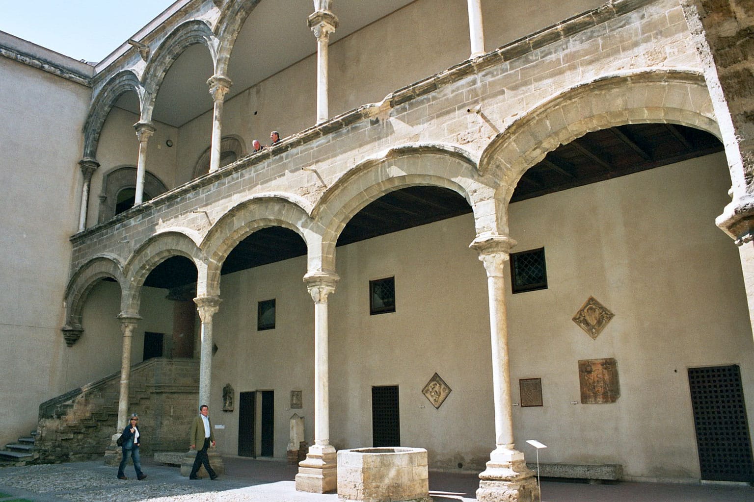 Innenhof des Palazzo Abatellis mit eleganten Steinbögen, einer oberen Galerie und Besuchern, die die historische gotisch-katalanische Architektur in Palermo erkunden.