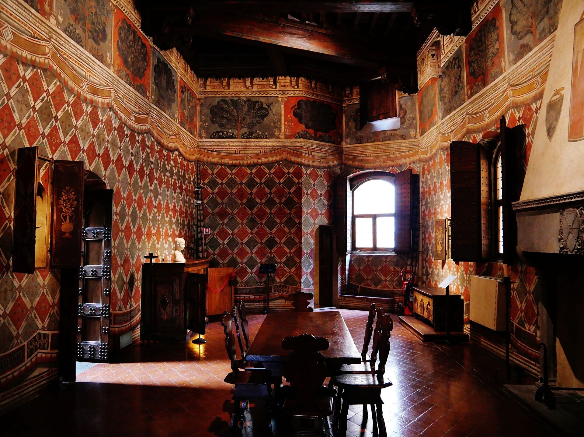 ห้องอาหารประดับประดาอย่างวิจิตรงดงามใน Palazzo Davanzati พร้อมผนังภาพเฟรสโกลวดลาย คานไม้ เฟอร์นิเจอร์โบราณ และแสงอาทิตย์ส่องผ่านหน้าต่างที่เปิดอยู่