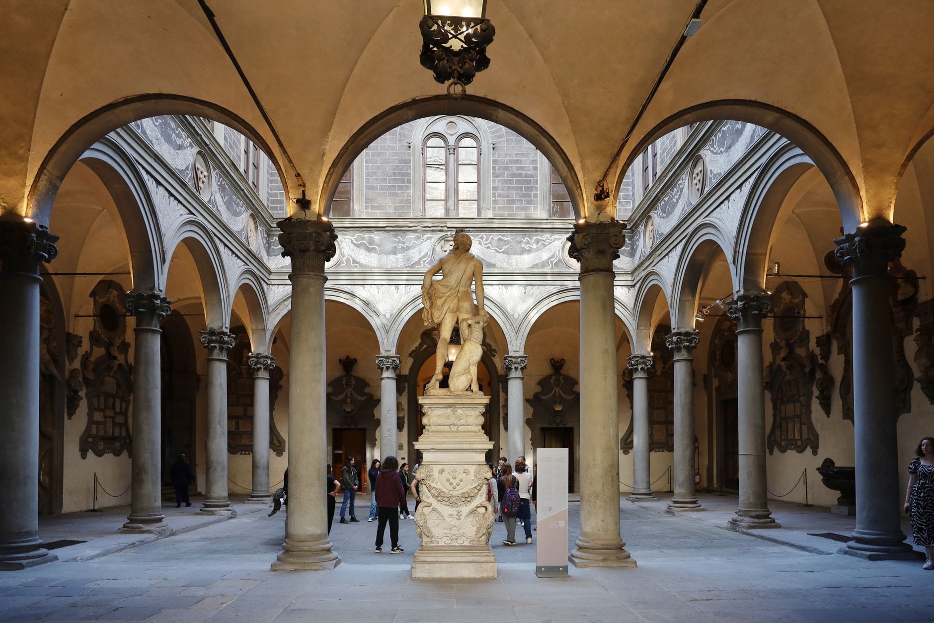 ลานกลางของ Palazzo Medici Riccardi ในเมือง Florence ที่มีโค้งประตูสไตล์เรเนสซองส์ เสาหิน รูปปั้นหินอ่อน และนักท่องเที่ยวที่เพลิดเพลินกับสถาปัตยกรรมอันทรงคุณค่าทางประวัติศาสตร์
