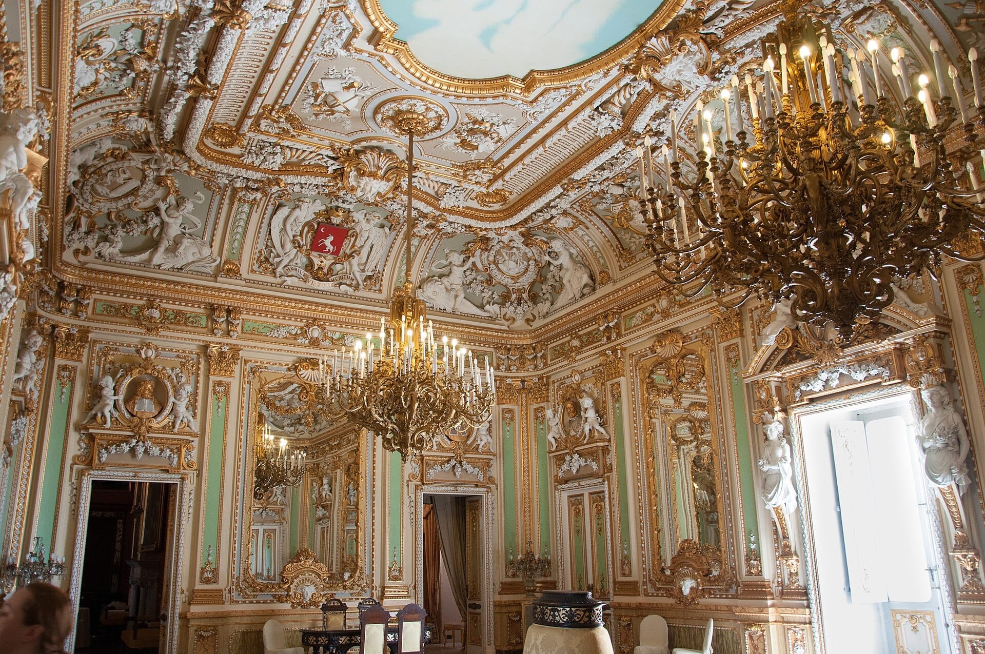 Sontuosa sala da ballo dorata nel Palazzo Parisio con stucchi barocchi, cornici dorate, grandi lampadari e pareti color pastello con statue classiche.