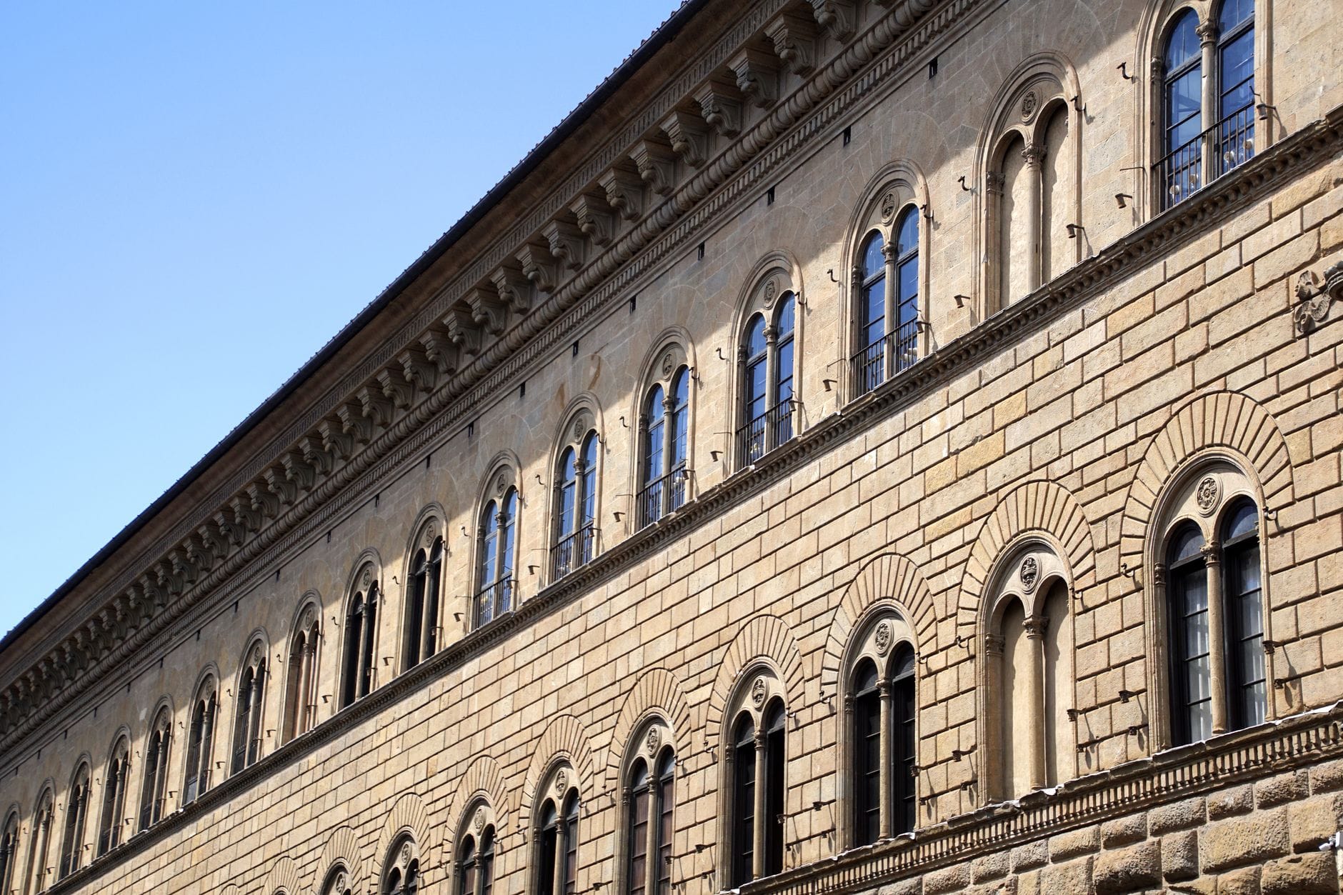 มุมมองด้านนอกของ Palazzo Strozzi กับผนังหินและแถวหน้าต่างโค้งสไตล์เรอเนสซองส์ ใต้ท้องฟ้าสีฟ้าใส