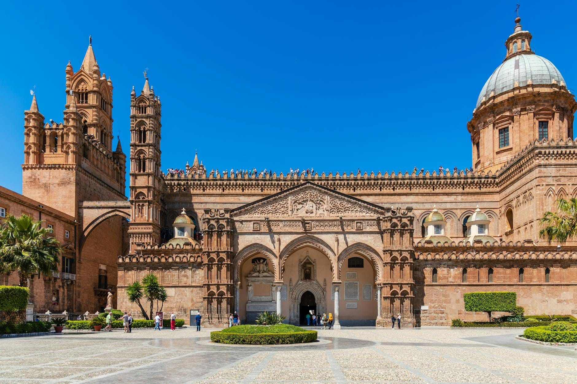 Weiter, sonniger Blick auf die prächtige Fassade der Kathedrale von Palermo mit Türmen, Bogeneingang und Kuppel vor strahlend blauem Himmel, Menschen auf dem weitläufigen Vorplatz.