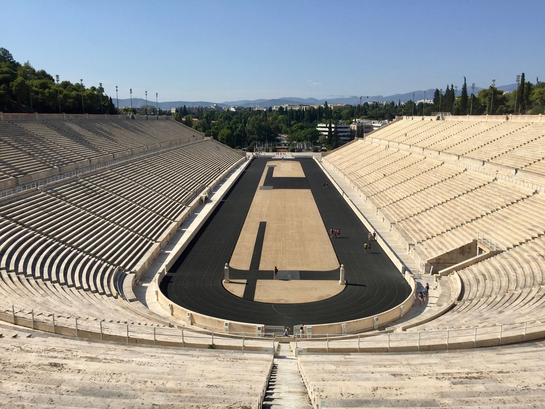 Vista grandangolare dello Stadio Panatenaico con le gradinate in marmo e la pista nera sotto un cielo azzurro terso, che restituisce tutta la grandiosità del luogo.