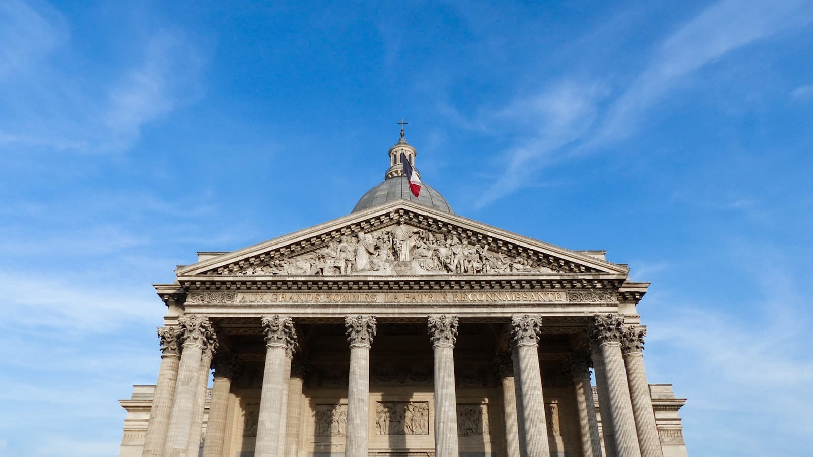 Vista frontale del Panthéon di Parigi con le colonne neoclassiche e la cupola su un cielo azzurro, ripresa in formato orizzontale.