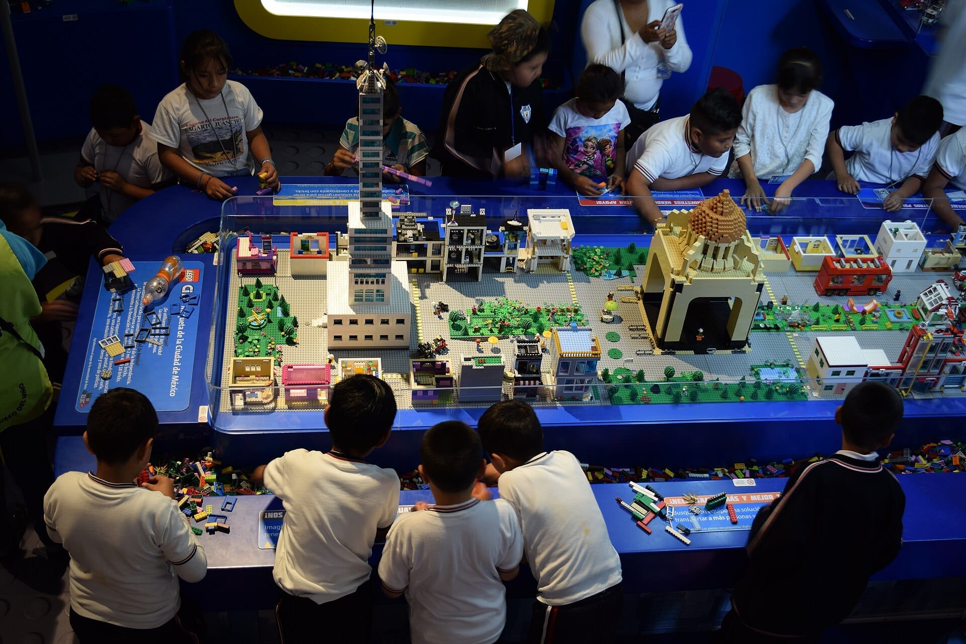 I bambini interagiscono con un dettagliato allestimento di città LEGO al Papalote Museo del Niño, con famosi monumenti di Città del Messico sotto una luminosa illuminazione interna.