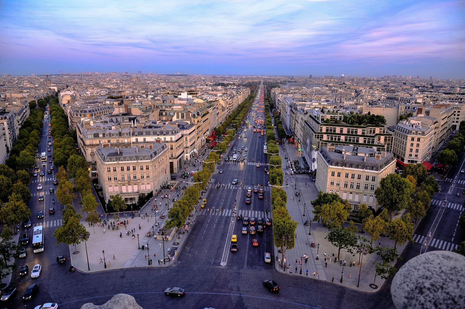 Ein weiter Blick die Champs-Élysées hinunter mit baumgesäumten Straßen und Stadtgebäuden bei Sonnenuntergang, gesehen vom Arc de Triomphe.