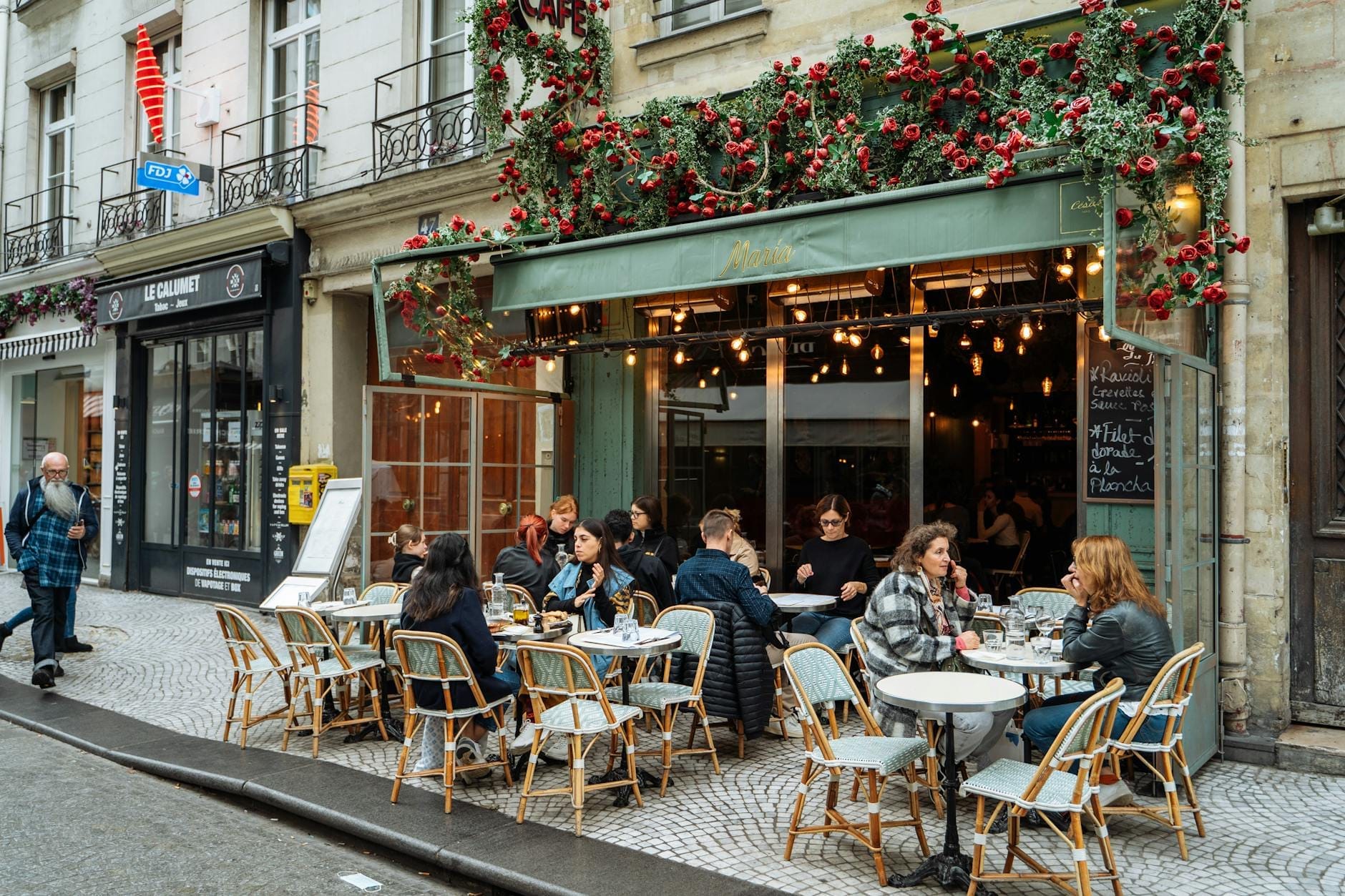 Menschen speisen im Freien in einem charmanten Pariser Café mit festlicher Dekoration und entspannter Atmosphäre, wobei gemütlicher Genuss im Vordergrund steht statt Museumsbesuche.