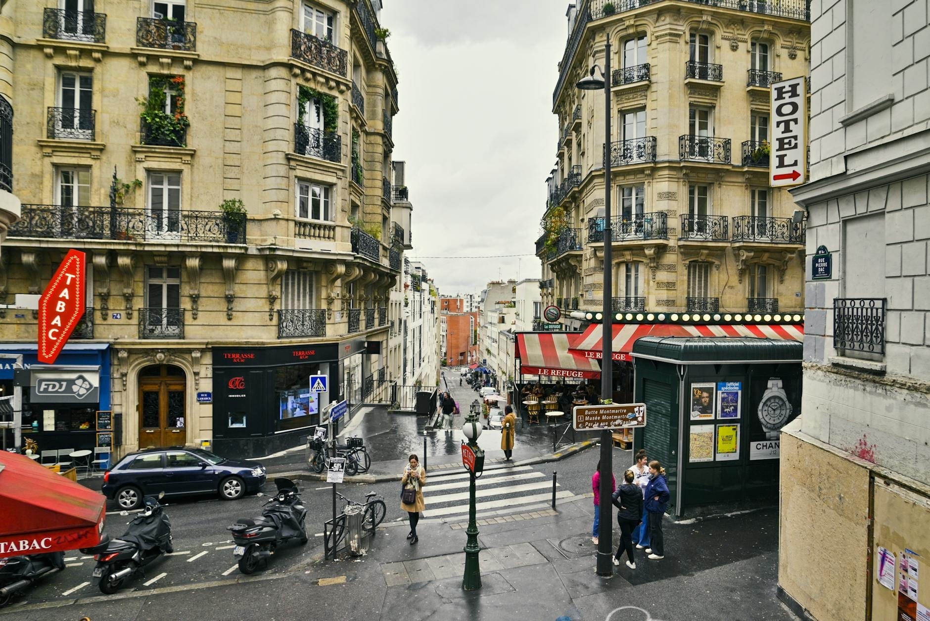 Scena di strada a Parigi con hotel, edifici classici e persone, che mostra diverse opzioni di alloggio in un vivace contesto urbano.