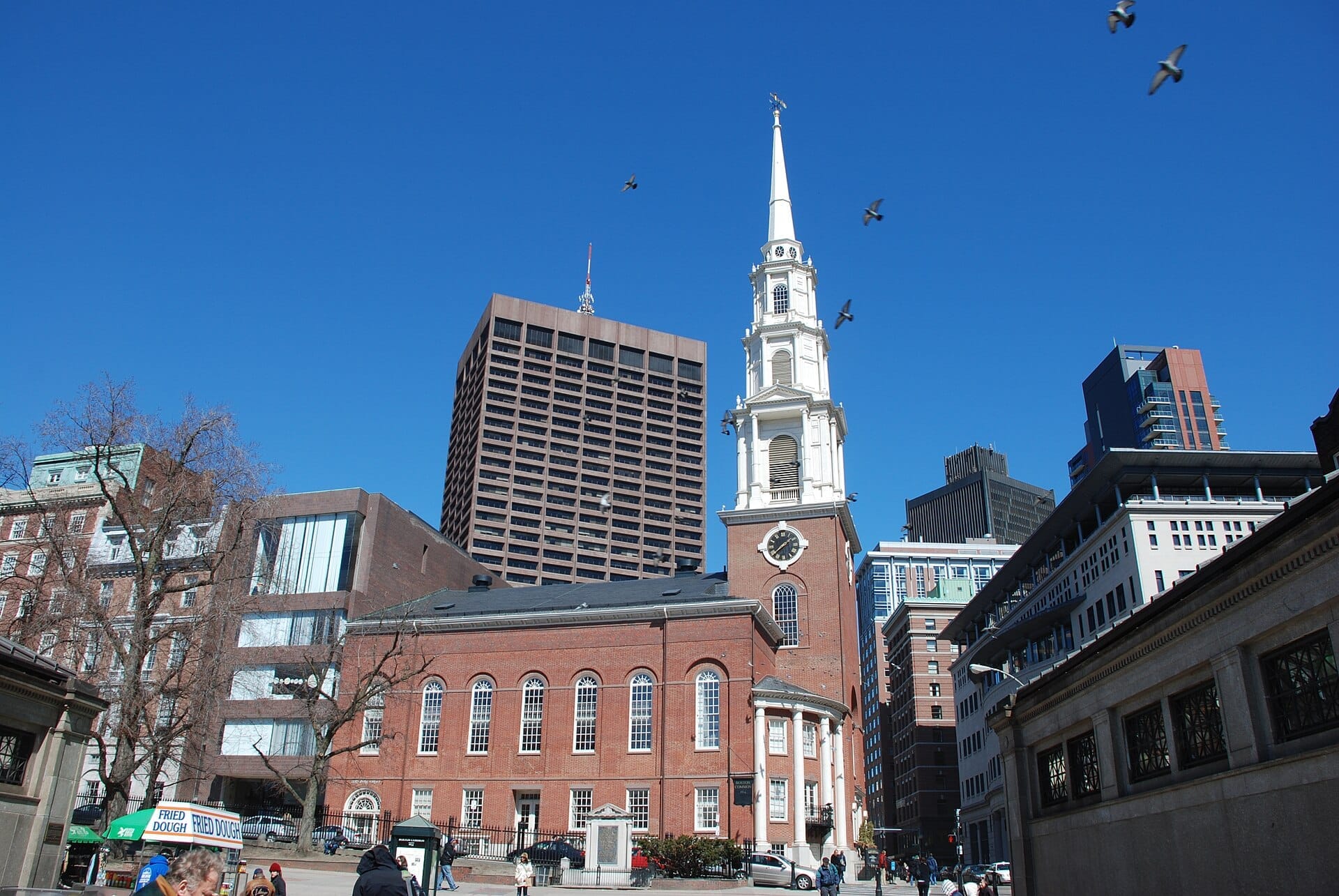 La Park Street Church con il suo campanile bianco spicca tra i moderni edifici di Boston sotto un cielo azzurro limpido, con persone che camminano nelle vicinanze.