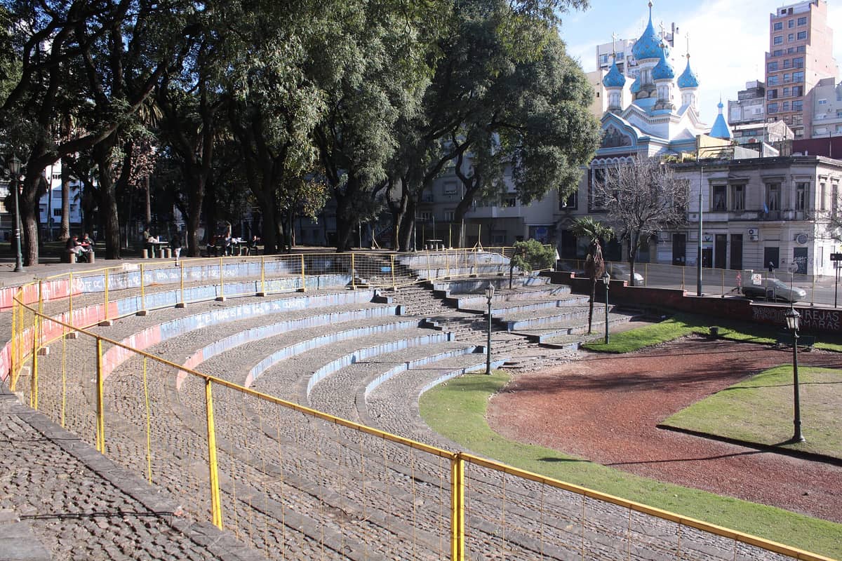 อัฒจันทร์กลางแจ้งใน Parque Lezama พร้อมม้านั่งหินโค้งเห็นโดมโบสถ์รัสเซียออร์โธดอกซ์เป็นฉากหลัง รายล้อมด้วยต้นไม้และตึกเมือง