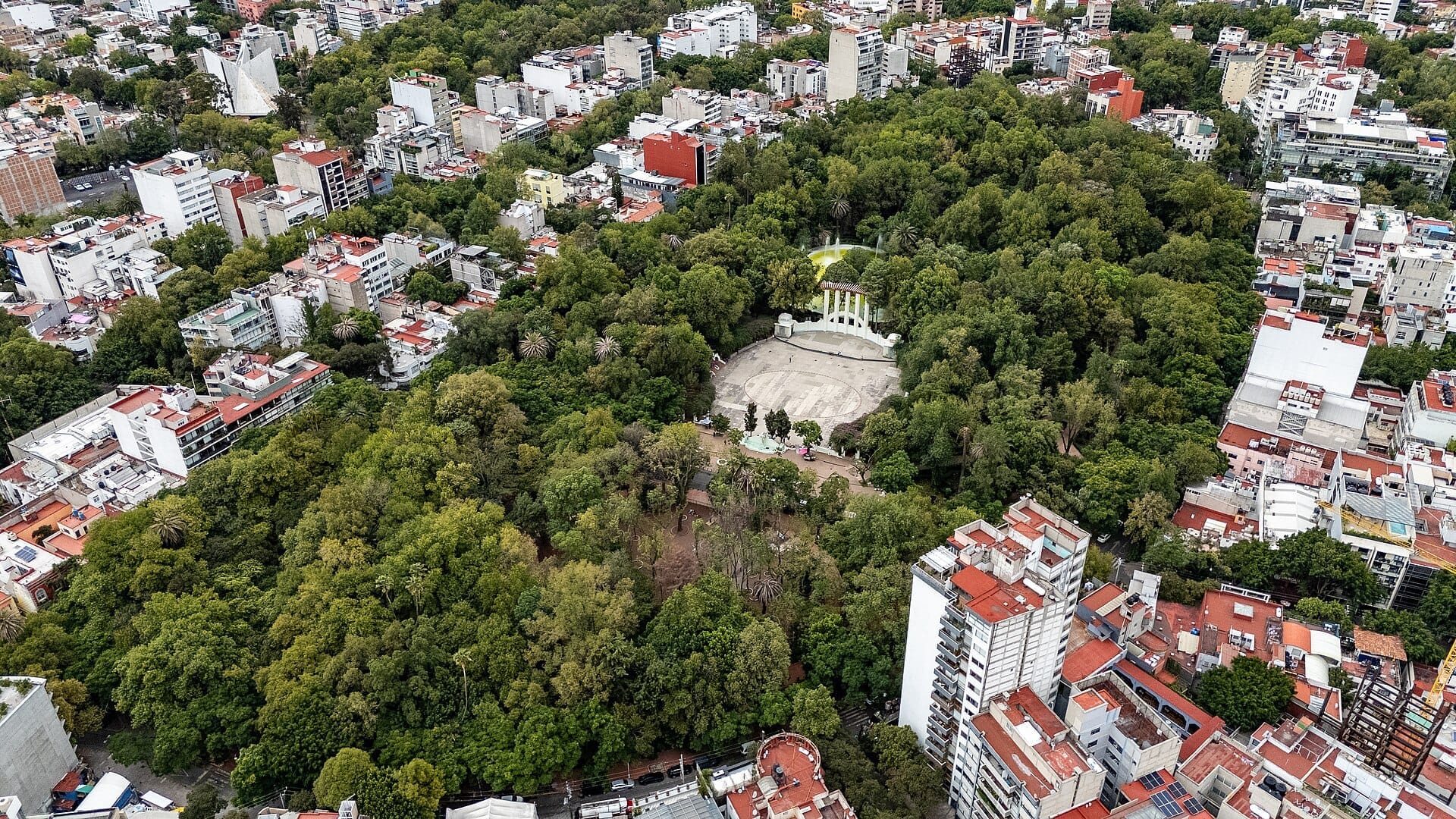 Vista aerea del Parque México nella Condesa, Città del Messico, con lussureggianti alberi verdi circondati da edifici urbani e il forum centrale in stile Art Déco.