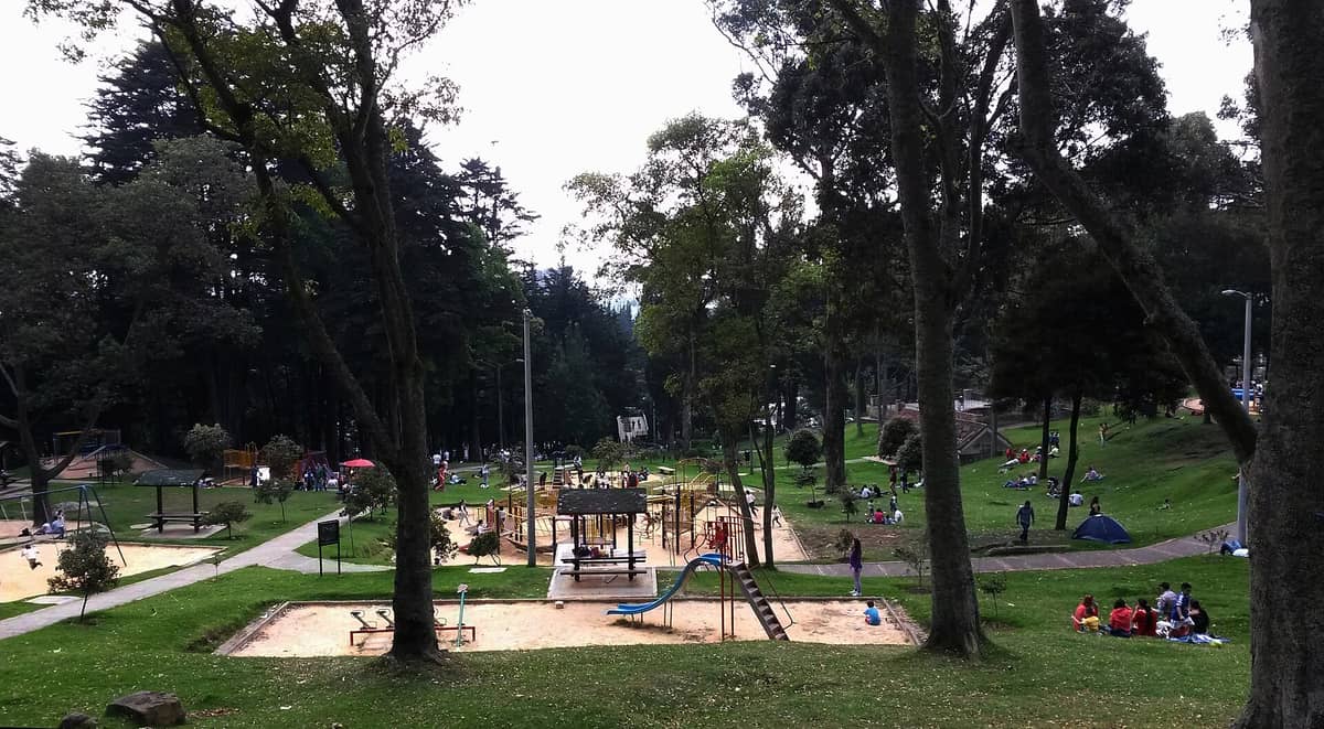 Playground and picnic areas surrounded by tall trees and families relaxing on the grass in Parque Nacional Enrique Olaya Herrera, Bogotá.