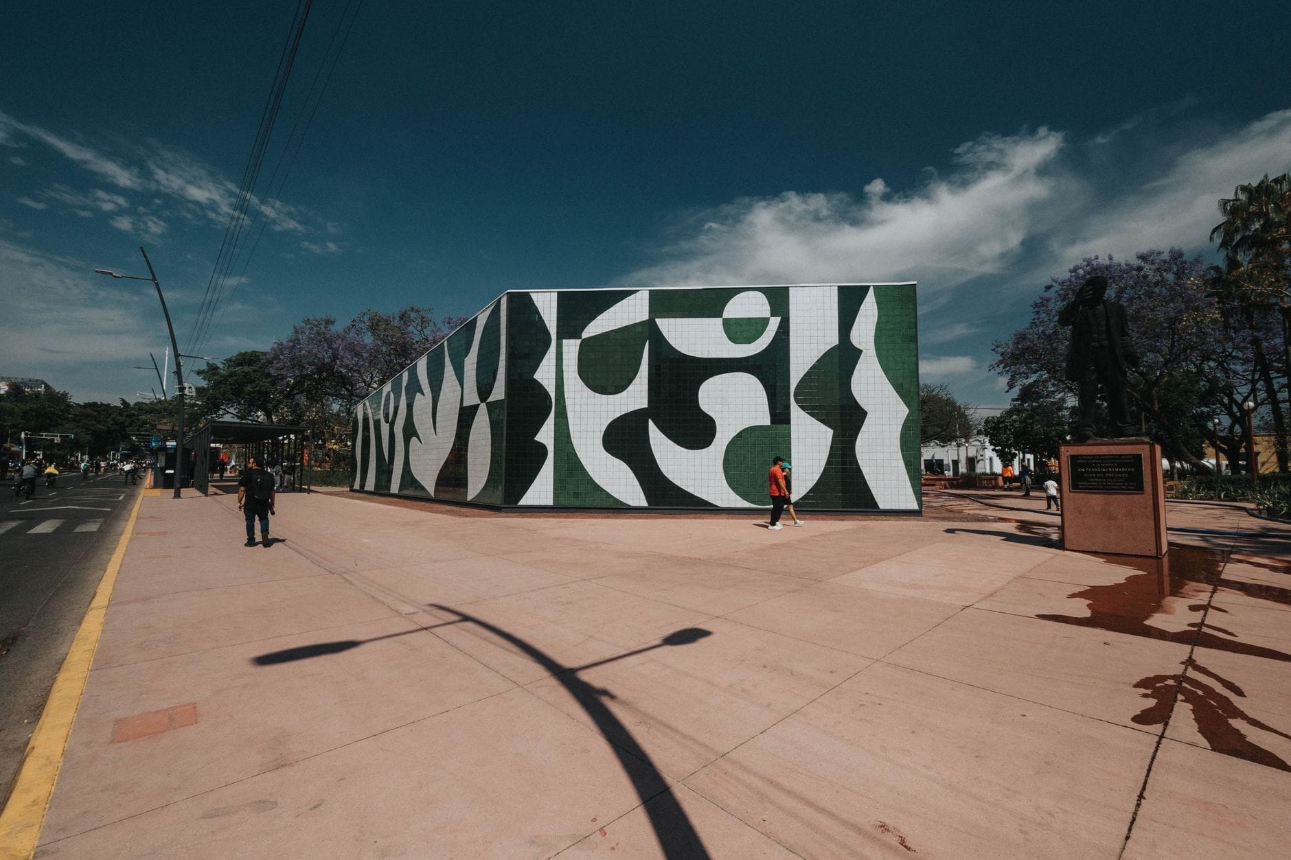 Statua davanti a un edificio con murale astratto verde e bianco al Parque Revolución, Guadalajara, sotto un cielo azzurro limpido.