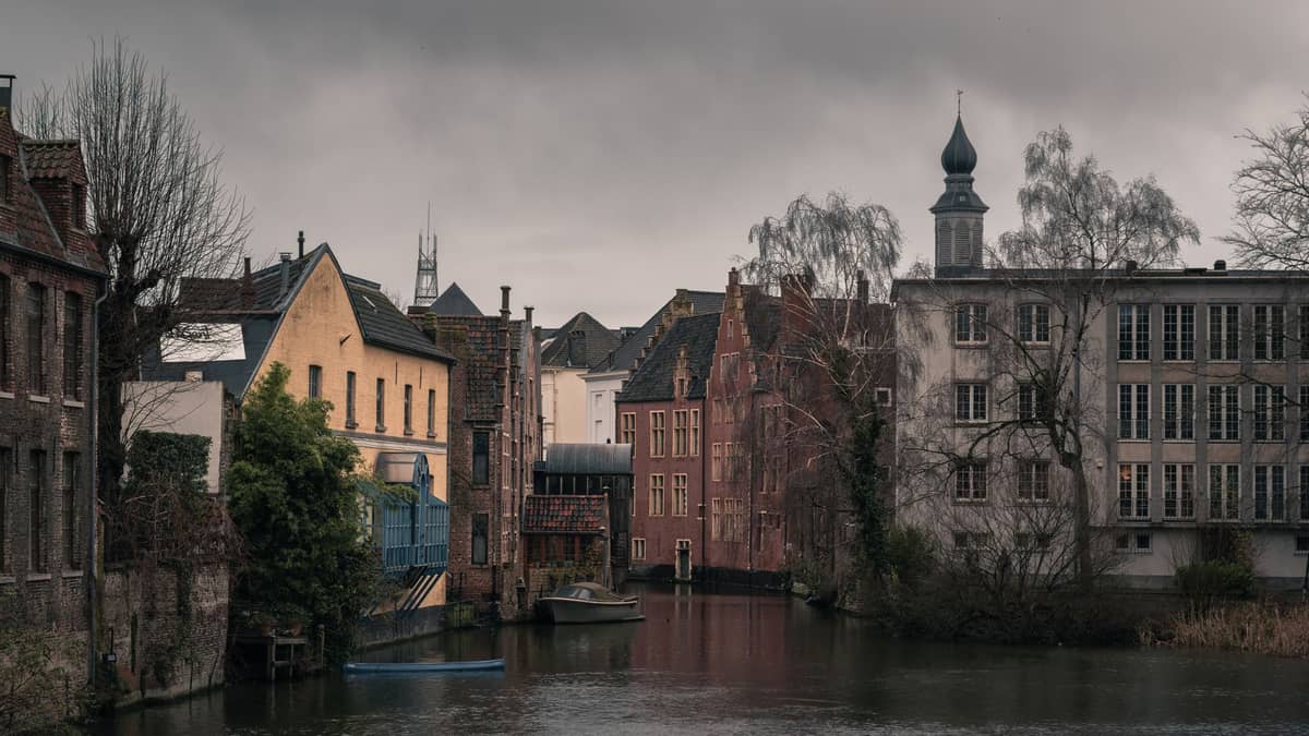 Atmospheric view of Patershol in Ghent showing historic medieval canal houses, calm waterway, and overcast sky, capturing the quiet character of the neighborhood.