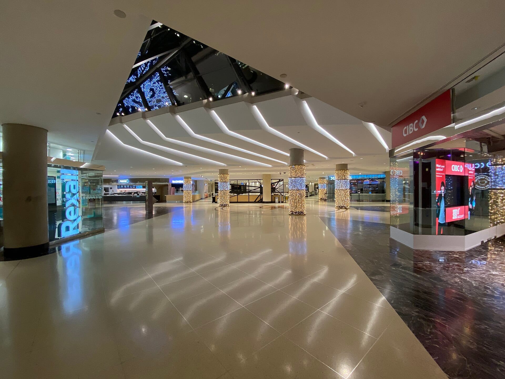 ทางเดินกว้างและทันสมัยภายใน PATH Underground City ของโตรอนโต มีแสงสว่างจ้า เสาที่ส่องสว่าง ร้านค้ากระจก และป้ายธนาคาร