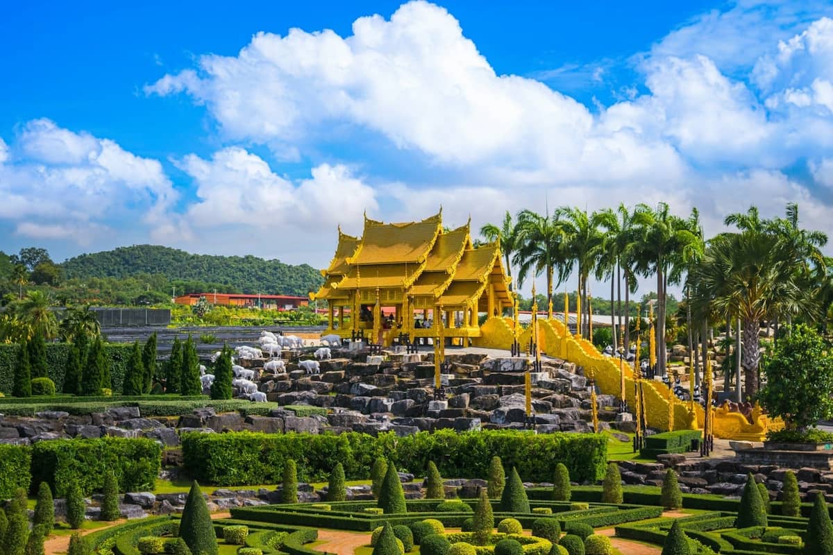 Beautifully landscaped garden in Pattaya featuring a golden Thai pavilion, palm trees, and manicured hedges under a bright blue sky.