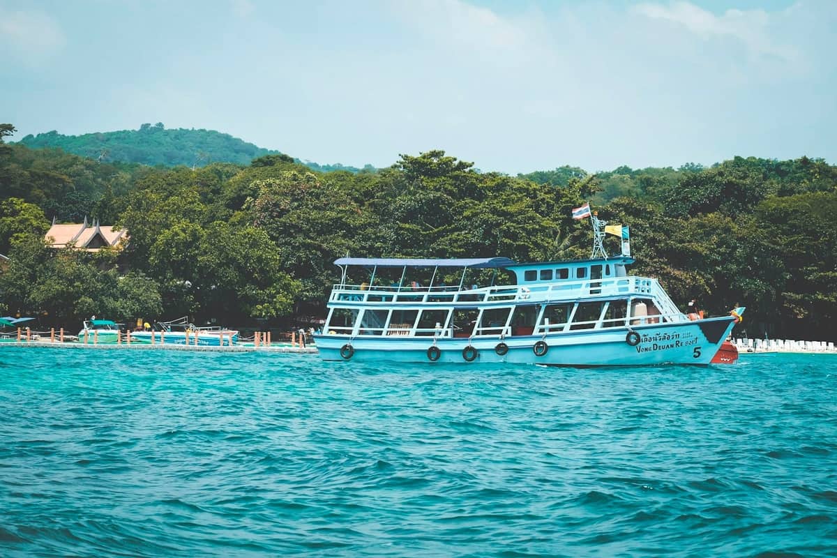 Turquoise ferry boat near the shore of a lush green island, with clear blue water and a partly cloudy sky.
