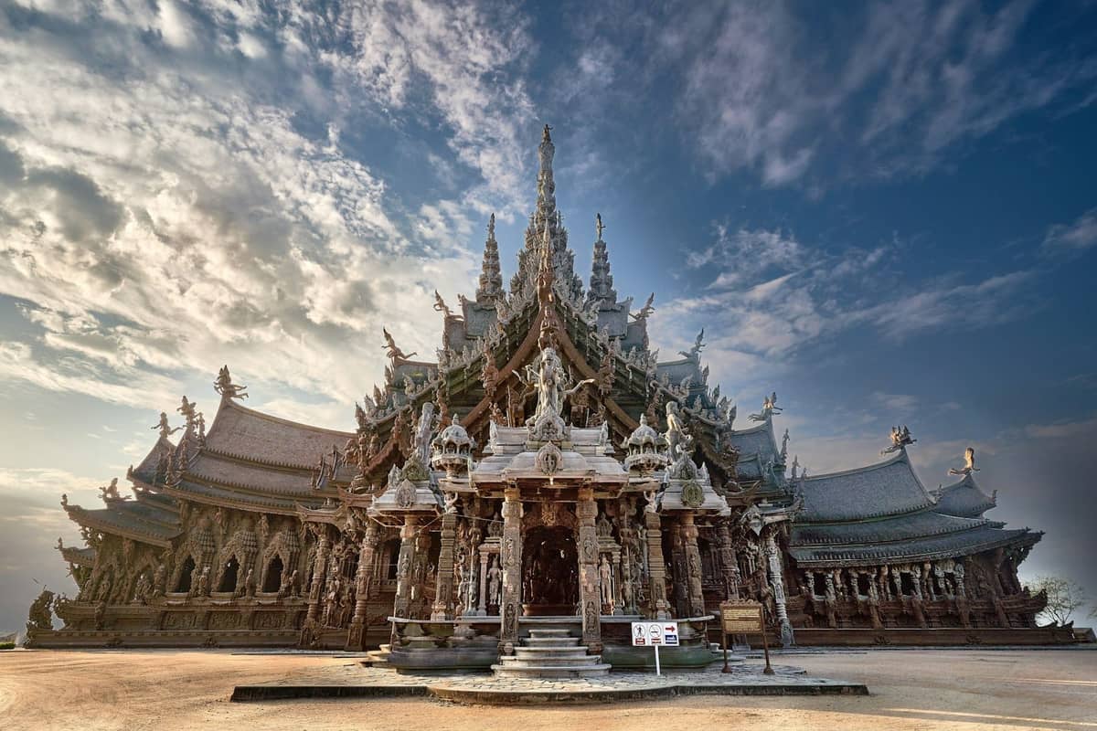 Wide view of the Sanctuary of Truth, a massive intricately carved wooden temple with dramatic spires under a partly cloudy sky.
