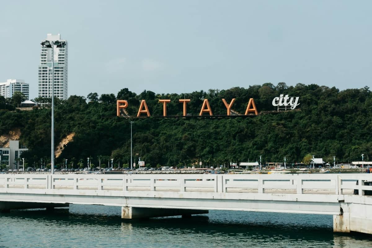 Wide view of the Pattaya City sign on a hillside with a pier and some tall buildings in the background.