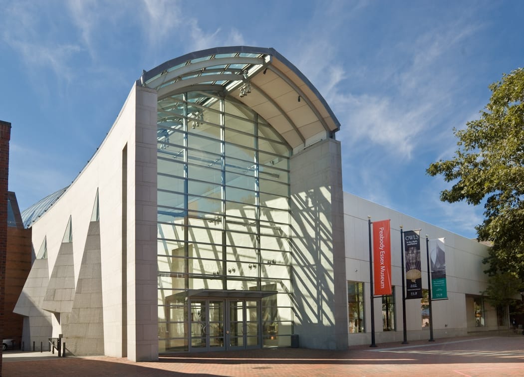 Ingresso moderno in vetro e pietra del Peabody Essex Museum a Salem, Massachusetts, con striscioni e cielo azzurro sullo sfondo.