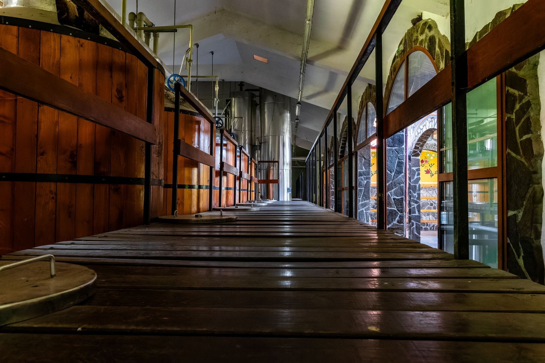 Interno di una distilleria con grandi vasche in legno e metallo, soffitto industriale e finestre ad arco in pietra, in un'atmosfera evocativa e suggestiva.
