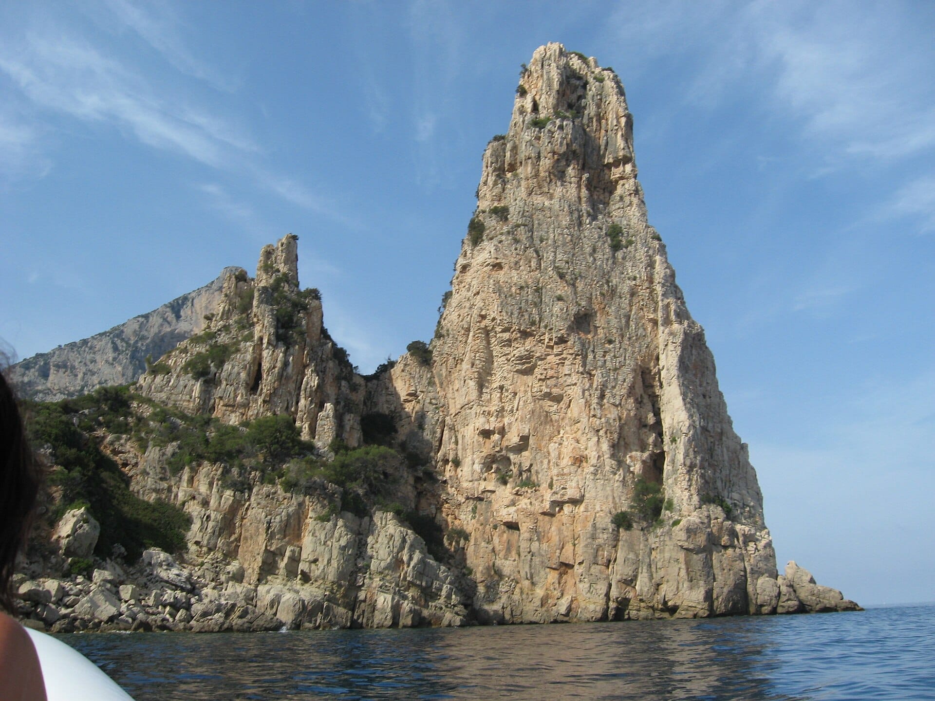 Pedra Longas aufragender Kalksteinfelsen erhebt sich direkt aus dem klaren blauen Tyrrhenischen Meer, mit schroffen Klippen und spärlichem Grün unter einem sonnigen Himmel.