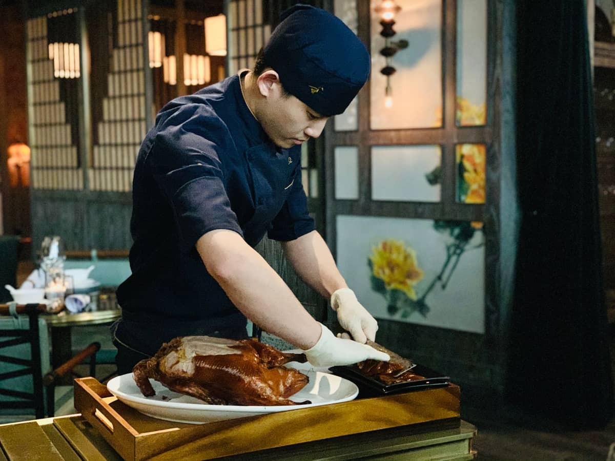 Koch tranchiert eine ganze Pekingente am Tisch in einem authentischen Restaurant – ein klassisches Bild des traditionellen Pekingenten-Erlebnisses in Peking.