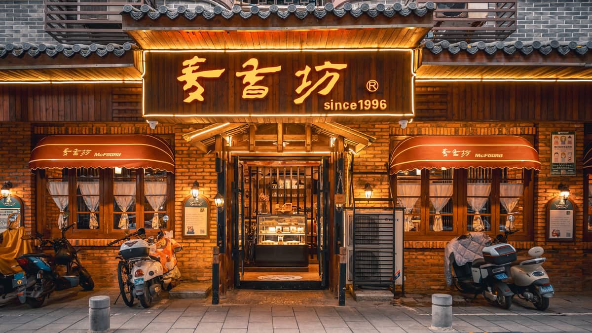 Warmly lit exterior of a traditional-looking Chinese restaurant with a large yellow sign and scooters parked out front at night.