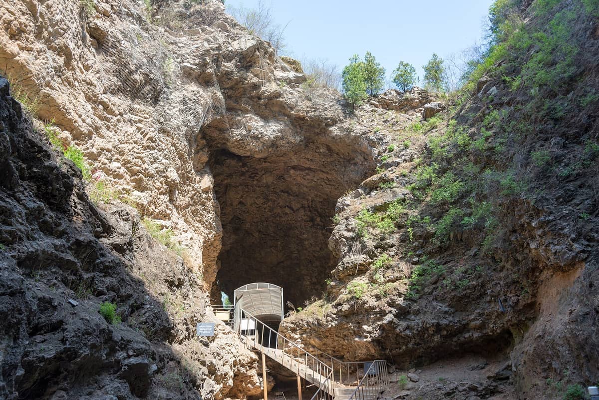 Eingang zur Höhle der Fundstätte des Peking-Menschen in Zhoukoudian, mit felsigen Kalksteinklippen und einer Treppe, die zur archäologischen Stätte führt.