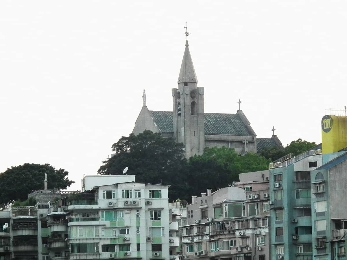 Blick auf die Kapelle Unserer Lieben Frau von Penha auf dem Penha Hill, die über Wohngebäuden und üppigen grünen Bäumen in Macau aufragt.
