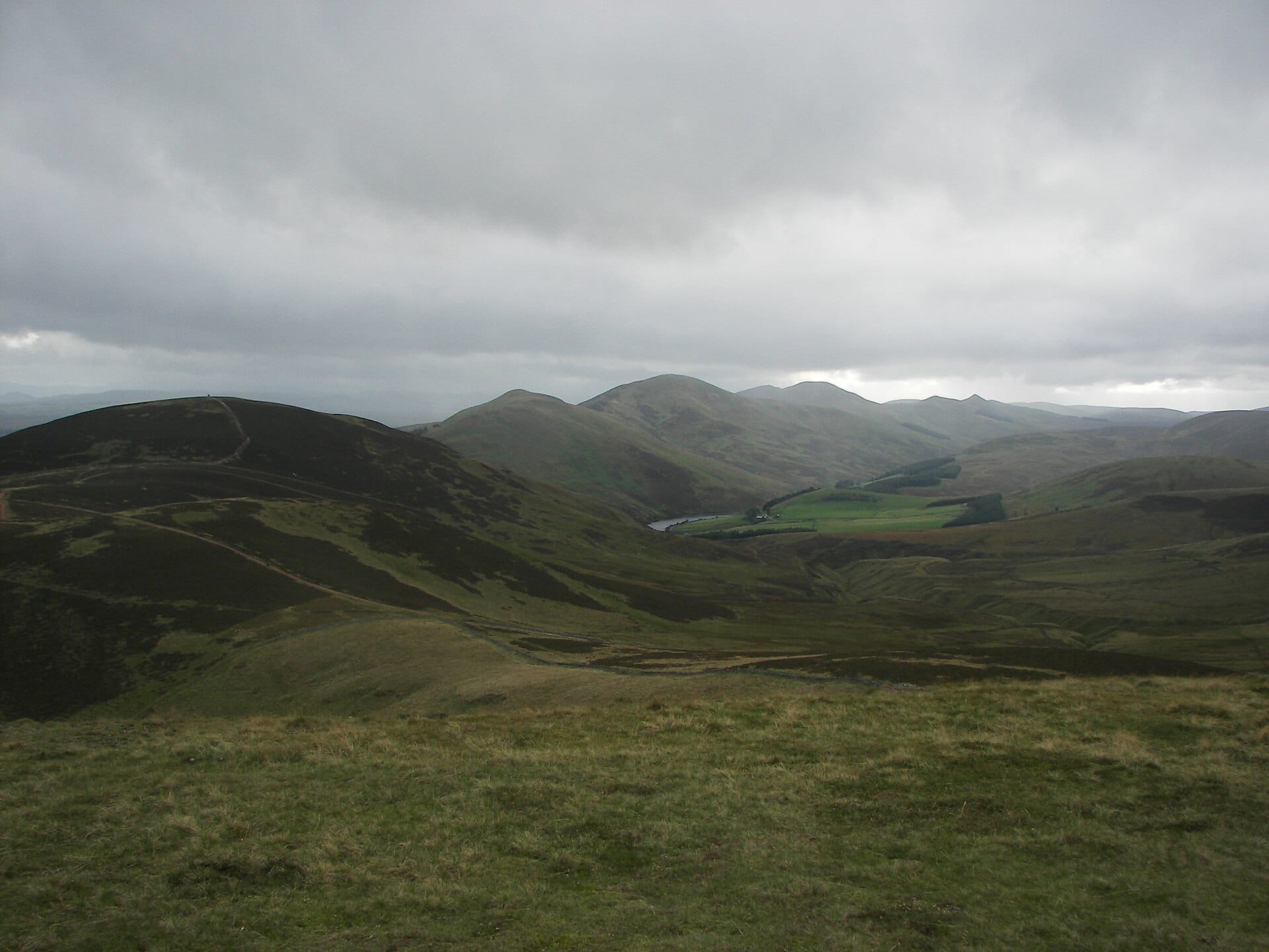 Sanfte grüne Hügel und gewundene Pfade unter einem bewölkten Himmel im Pentland Hills Regional Park nahe Edinburgh, Schottland.