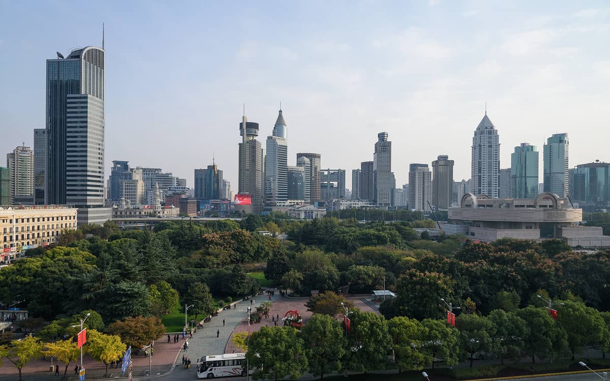 Weitläufige Luftaufnahme des Volksplatzes in Shanghai mit Grünflächen, belebten Spazierwegen, dem Shanghai-Museum und modernen Wolkenkratzern im Hintergrund.