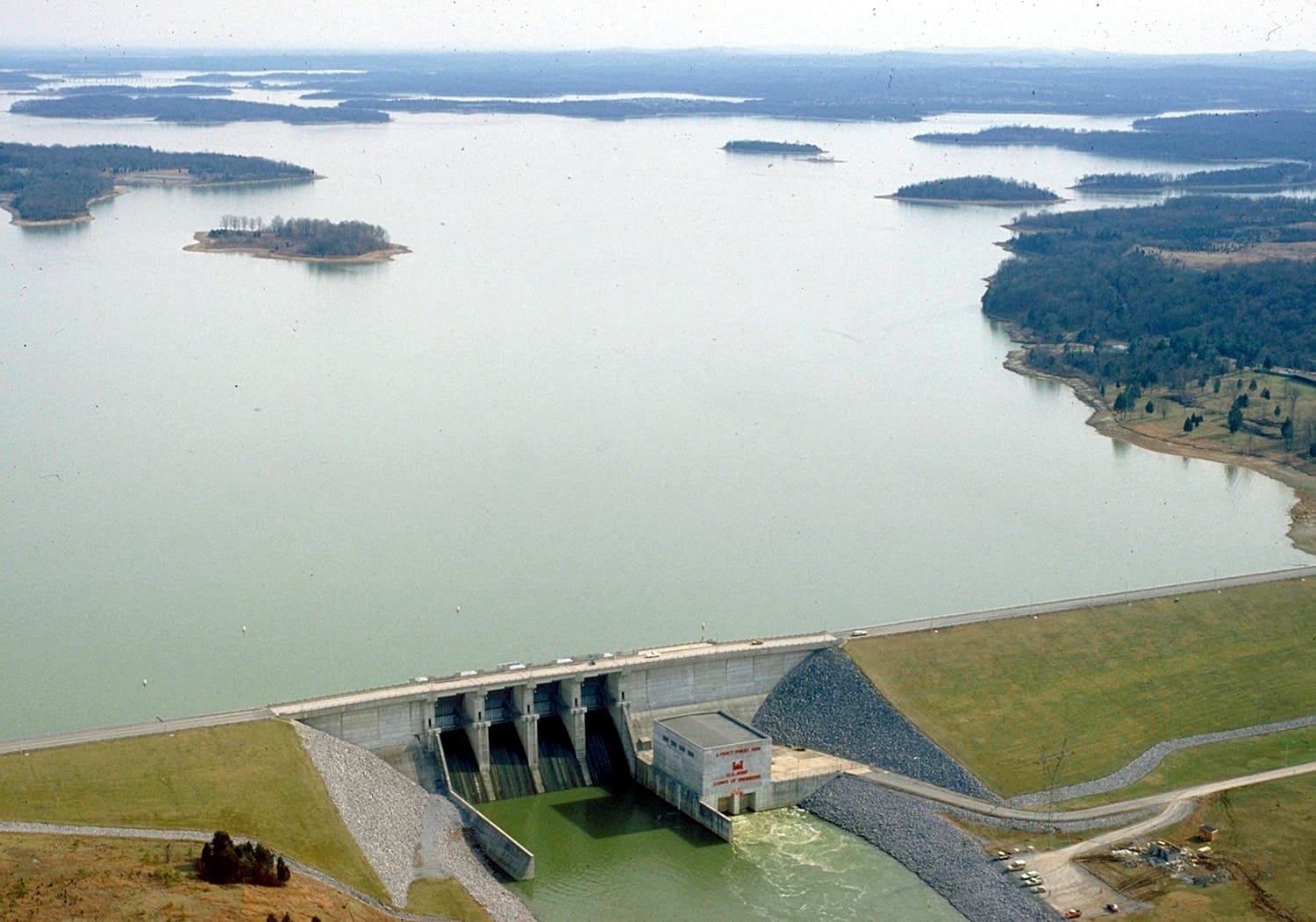 Vista aérea del lago J. Percy Priest que muestra el extenso embalse, las islas boscosas circundantes y la estructura de la presa de hormigón en primer plano.