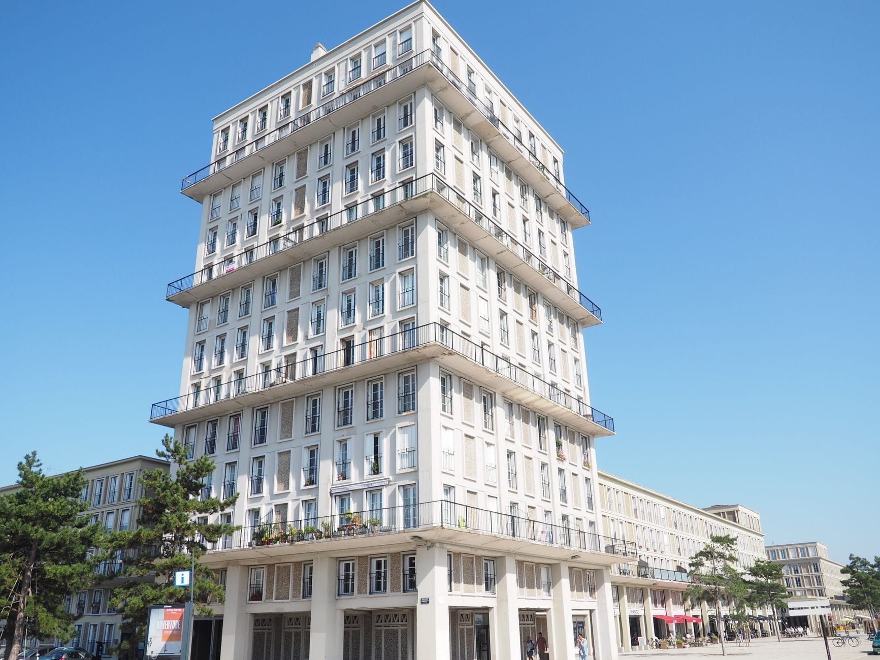 Bloque de apartamentos modernista luminoso en el barrio Perret de Le Havre bajo un cielo azul, con líneas geométricas y fachada de hormigón pálido.