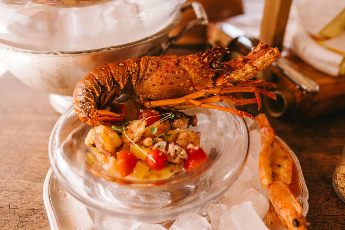 Cooked rock lobster served on a glass bowl with a seafood salad, surrounded by ice and prawns.