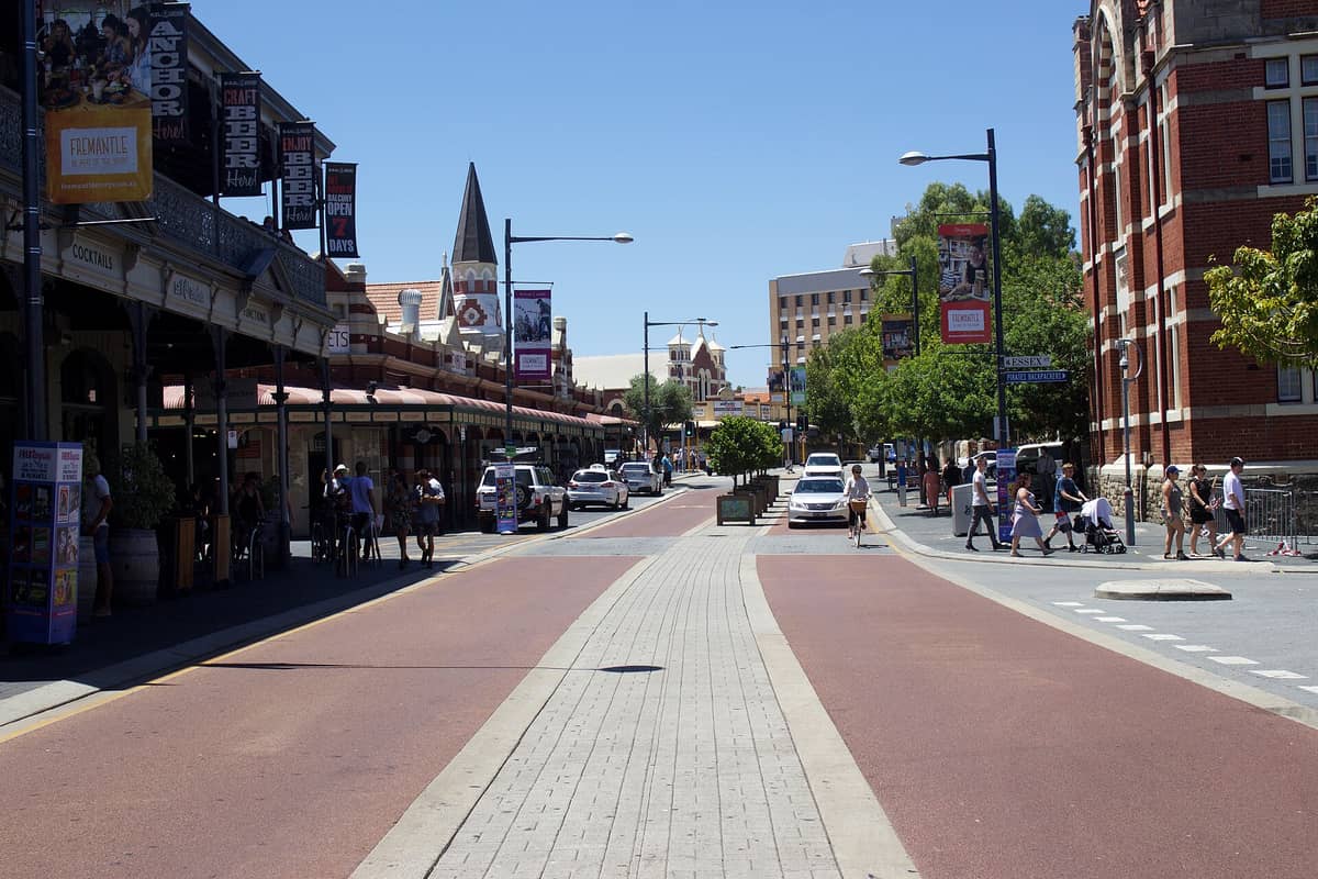 Die belebte South Terrace in Fremantle, gesäumt von Cafés und Restaurants, mit Fußgängern und geparkten Autos entlang der Straße an einem sonnigen Tag.
