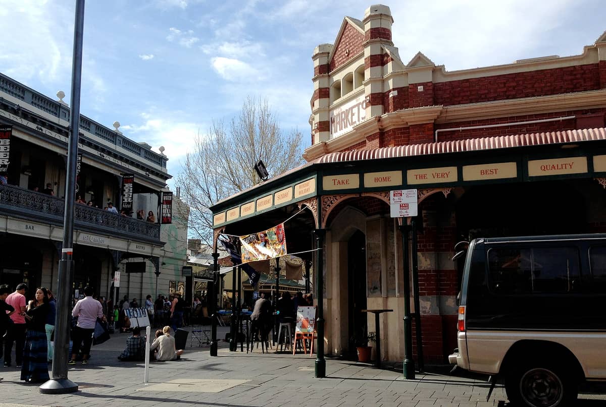 Backsteinvorderseite der Fremantle Markets mit Menschenmengen draußen an einem sonnigen Tag, was einen Eindruck von den Marktzeiten und den belebten Perioden vermittelt.