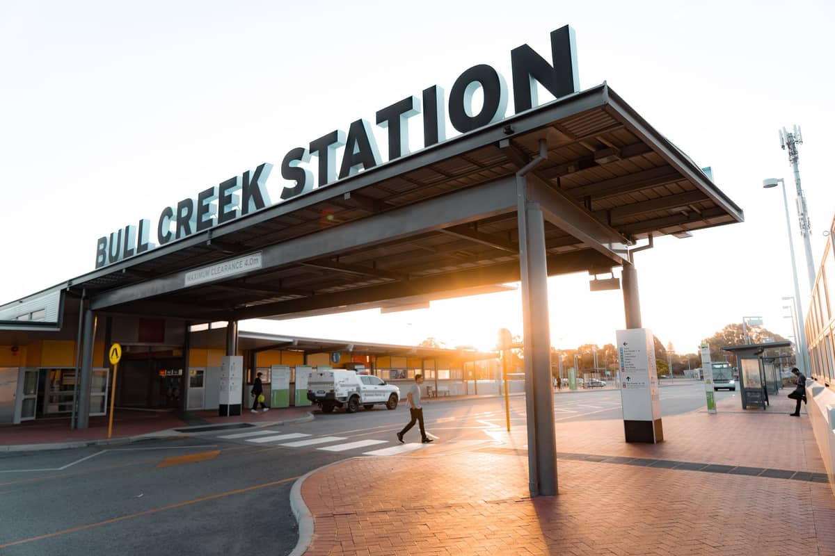 Entrada a la estación Bull Creek en Perth con luz solar y personas, mostrando acceso al transporte público.