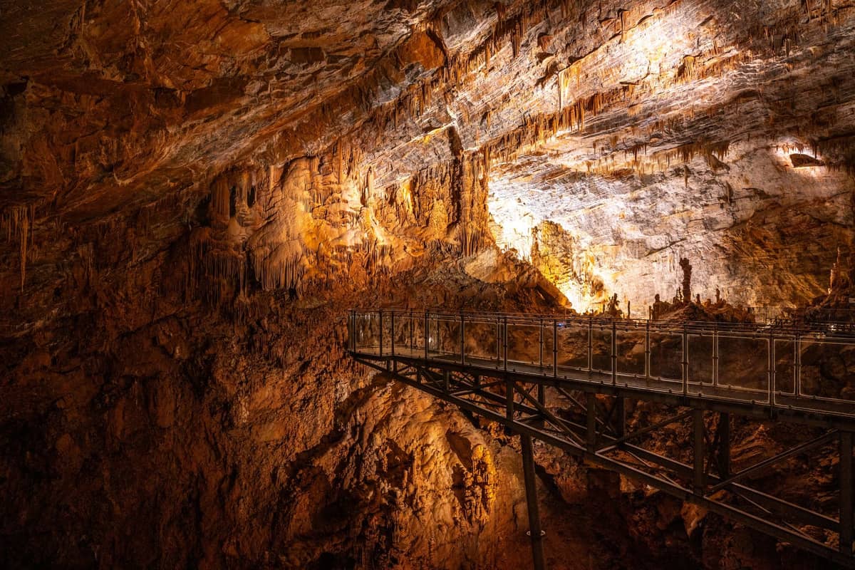 Gran cueva de piedra caliza iluminada con un puente peatonal, con estalactitas y formaciones rocosas, típica de las famosas cuevas de Margaret River.