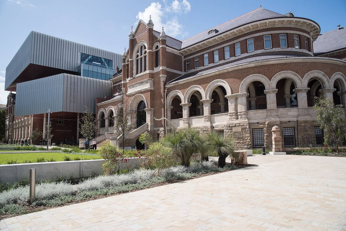 Nowoczesna i historyczna architektura WA Museum Boola Bardip w Perth Cultural Centre – główne wejście i zagospodarowany dziedziniec na tle błękitnego nieba.