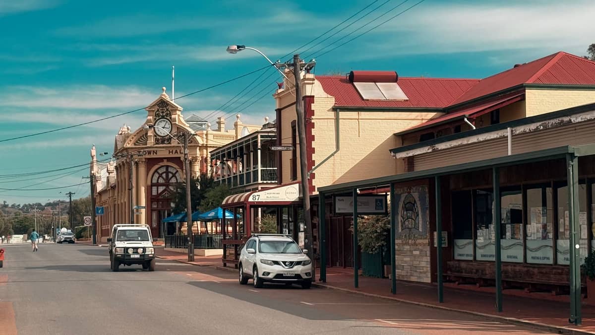 Ein historisches Rathaus und eine Hauptstraßenszene in einer kleinen australischen Landstadt, mit Gebäuden im Kulturerbe-Stil und geparkten Autos unter blauem Himmel.