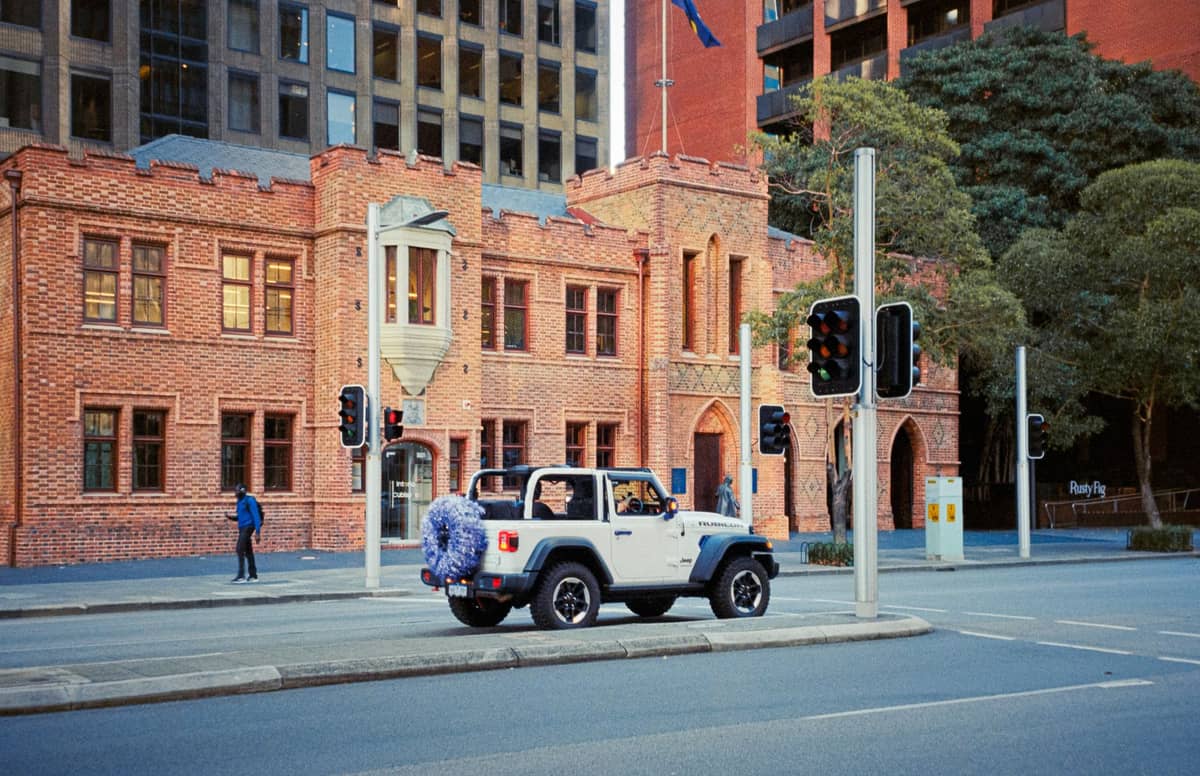 Rotes Backsteingebäude mit Zinntürmen an einer Stadtstraße in Perth, Australien, mit Ampeln und einem davor geparkten weißen Jeep.