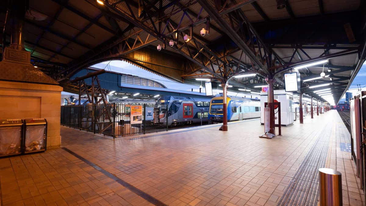 Weitwinkelansicht eines gut beleuchteten Bahnsteigs in Perth bei Nacht mit einem modernen Transperth-Zug, der unter einem großen Metalldach hält.