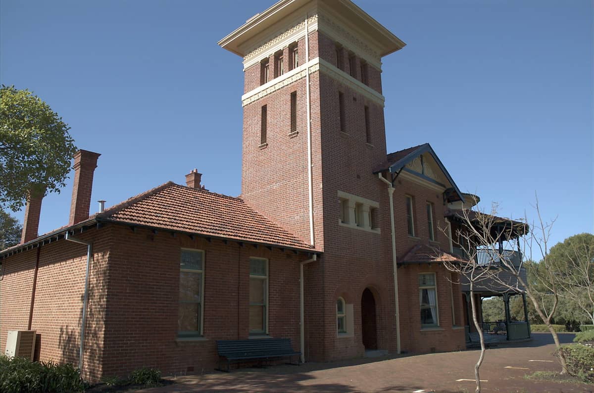 Historisches Backsteingebäude mit Turm des Perth Observatory in den Perth Hills, aufgenommen unter einem klaren blauen Himmel, umgeben von Bäumen.